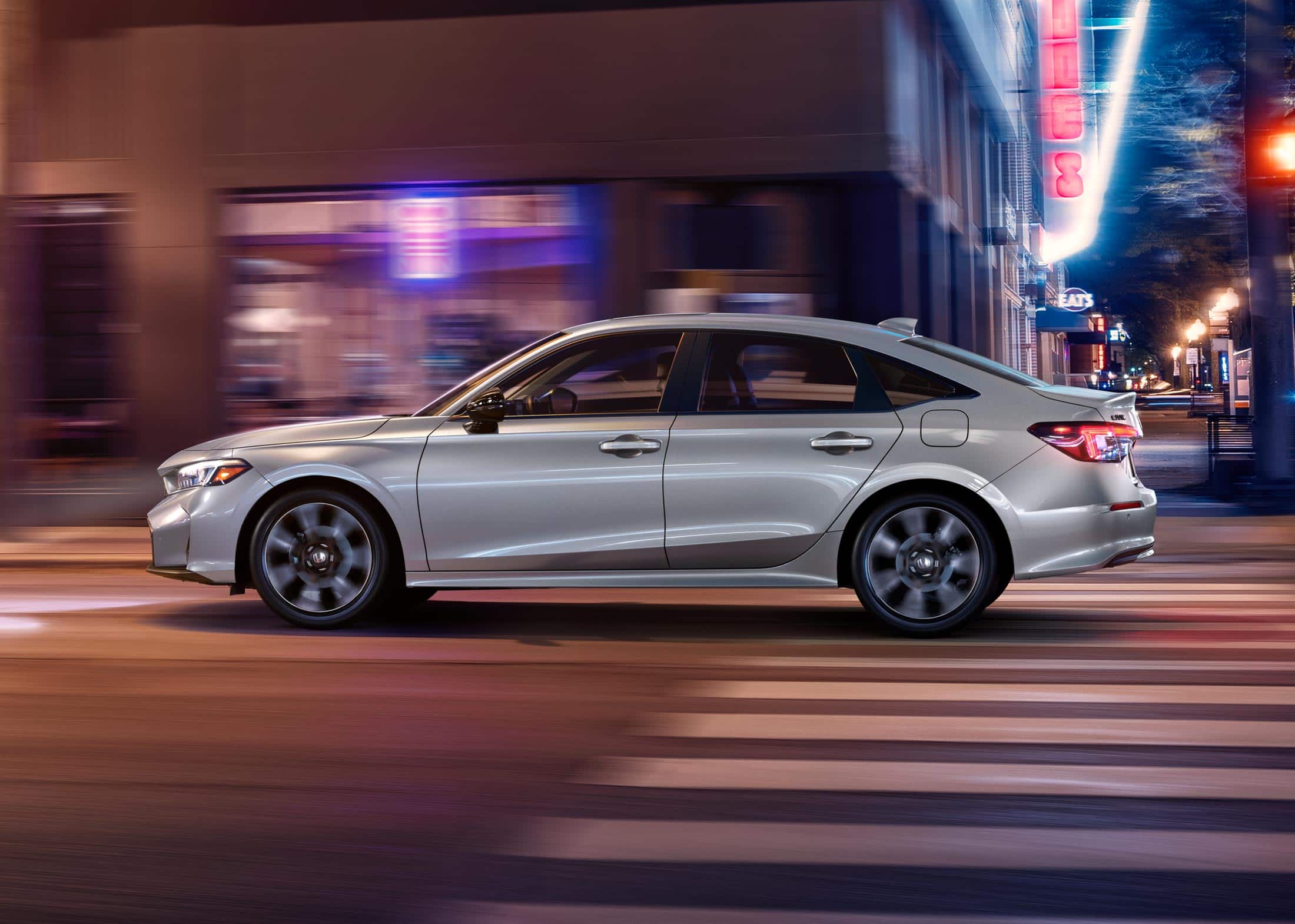 2026 Honda Civic Sedan Sport Touring Hybrid in Solar Silver Metallic side profile driving on a city street (Compact Sedan)