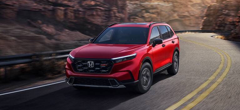 2027 Honda CR-V TrailSport Hybrid in Radiant Red Metallic front driving on a winding mountain road (Compact Crossover SUV). 2027 Honda CR-V TrailSport Hybrid in Radiant Red Metallic front driving on a winding mountain road (Compact Crossover SUV).
